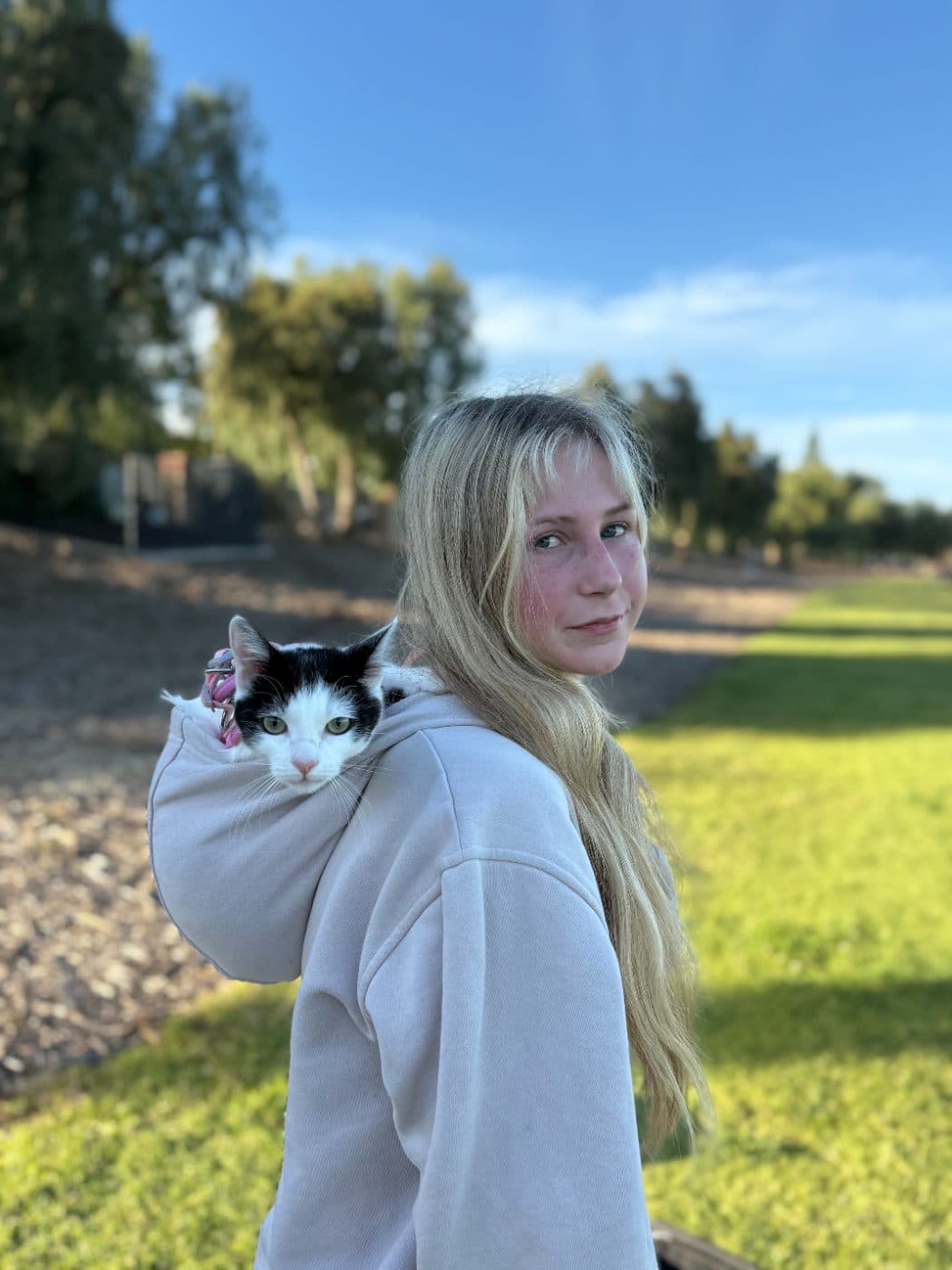 Brianna carrying a black and white cat in her hoodie at a park in Thousand Oaks, ready for a cat sitting visit